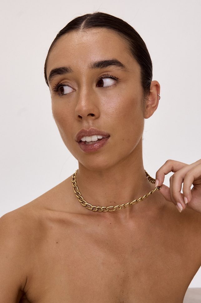 Model looking away and holding a gold chunky bold chain statement necklace from australian online store Martini Street which sells waterproof, high quality jewellery.