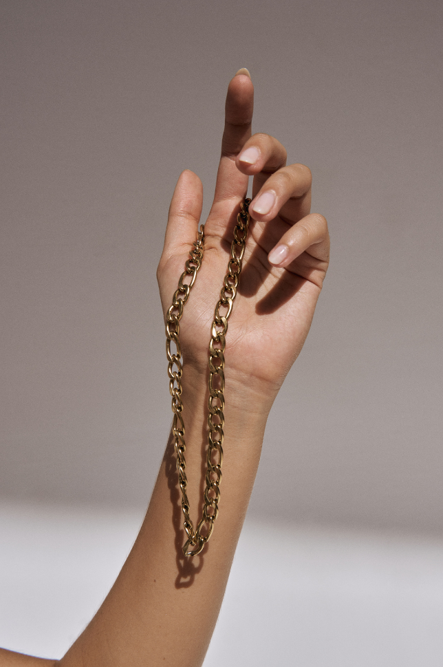 Hand model holding a gold chunky bold chain statement necklace from australian online store Martini Street which sells waterproof, high quality jewellery with light pink almond shaped nails.