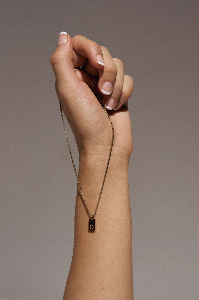 Hand model holding a gold initial letter pendant necklace from australian online store Martini Street which sells waterproof, high quality jewellery.