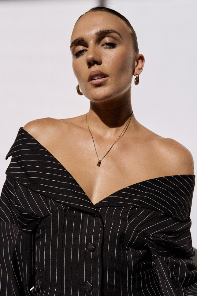 Woman wearing a gold initial letter pendant necklace with black outfit from australian online store Martini Street which sells waterproof, high quality jewellery.